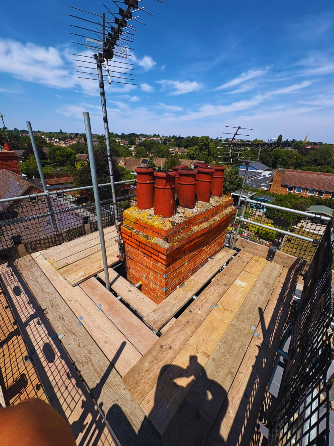 Chimney scaffold decking around a tall stack with pots, guardrails and netting