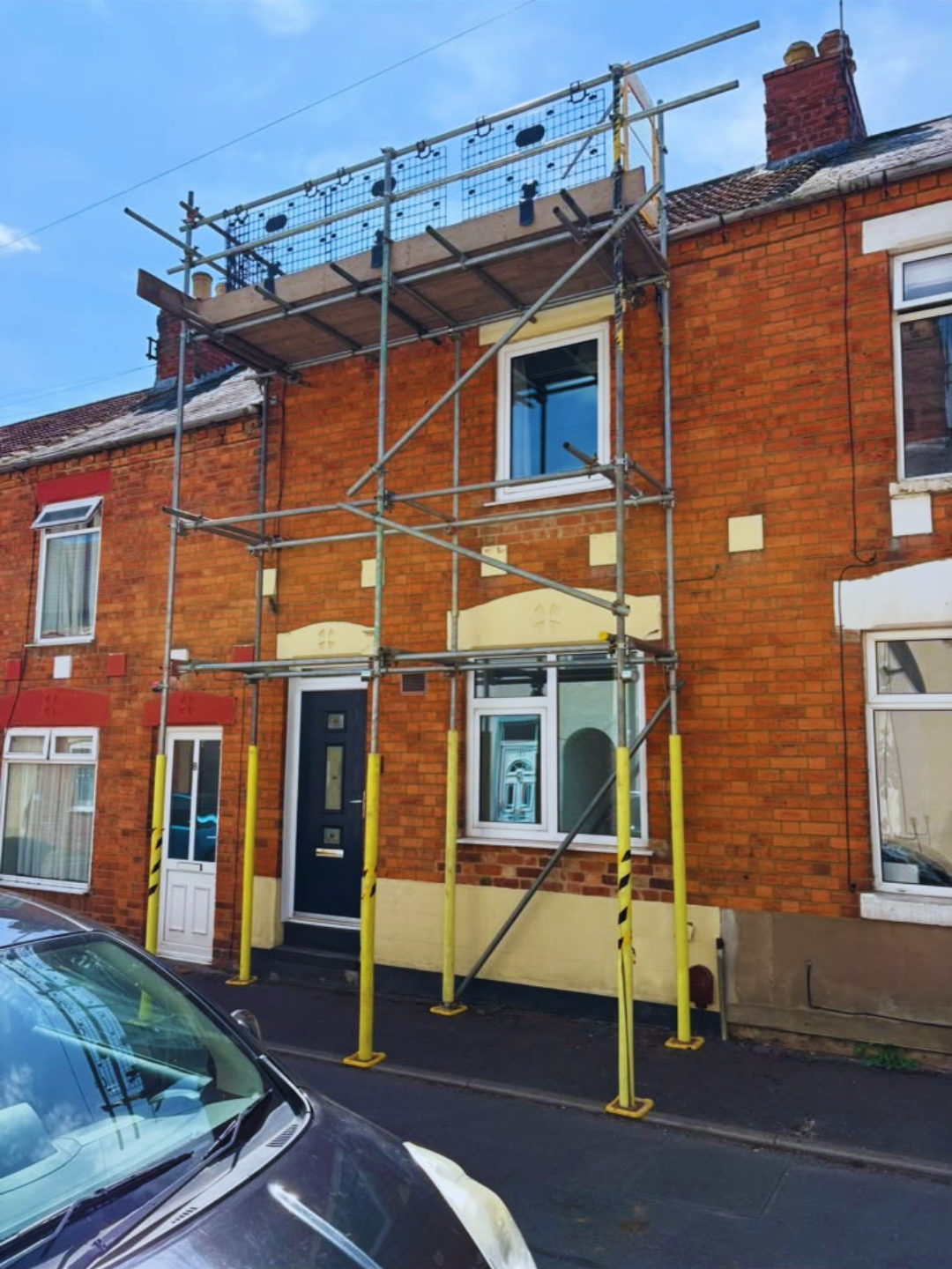 Pavement scaffolding to a terraced house with padded uprights on the footway